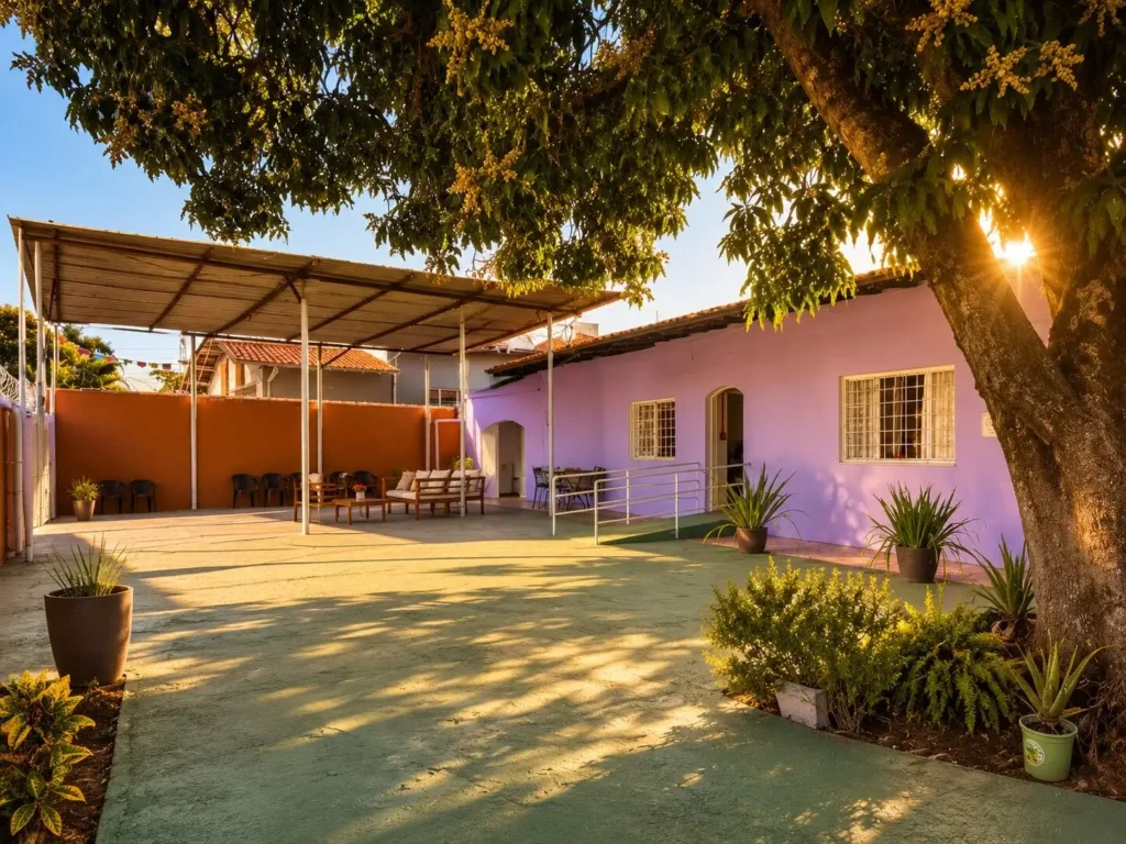 Fachada da casa em lilás vista do pátio, com rampa de acesso, área coberta à esquerda e vasos de plantas